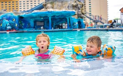 Two happy children wearing colorful arm floaties in the crystal blue pool at Margaritaville Resort Biloxi