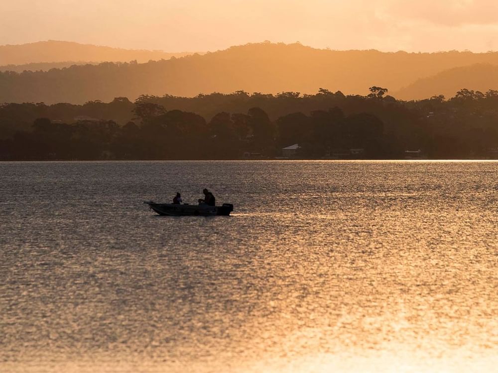 Small boat with two people on a golden shimmering lake near Mercure Kooindah Waters