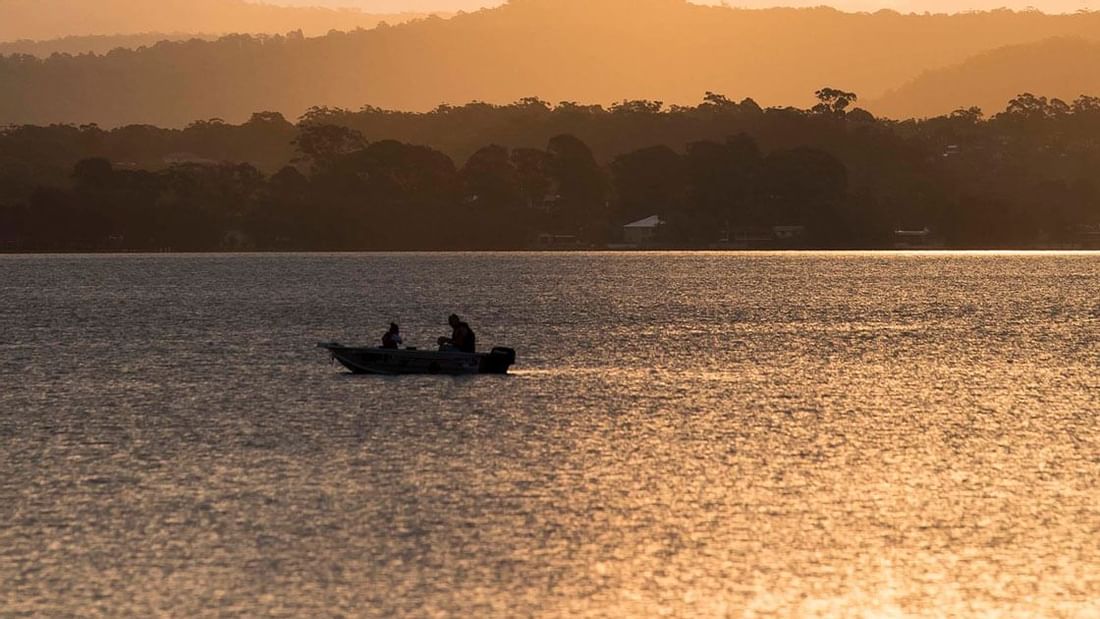 Small boat with two people on a golden shimmering lake near Mercure Kooindah Waters