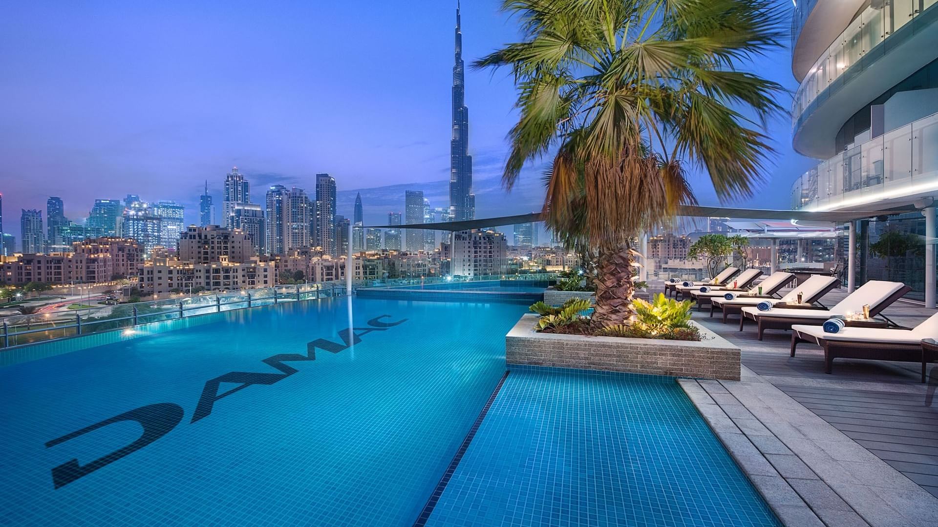 An outdoor pool on a terrace with sun loungers and the view of Burj khalifa from the DAMAC Maison Distinction