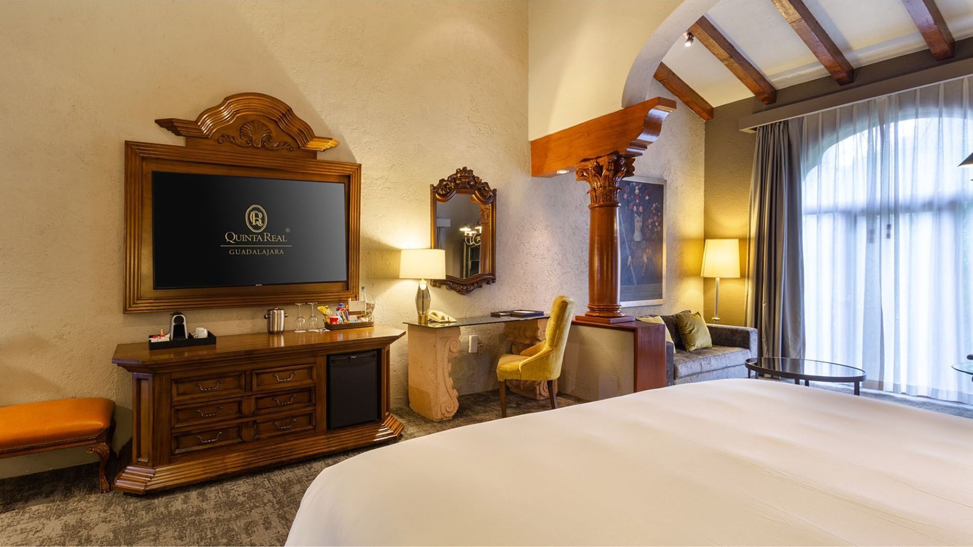 King Grand Class suite with a wooden TV console and a decorative column, found at the Quinta Real Guadalajara