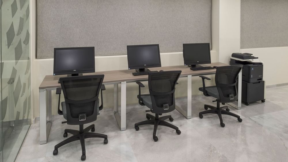 Business center equipped with three computer stations, ergonomic chairs, and a printer at Real Inn Celaya