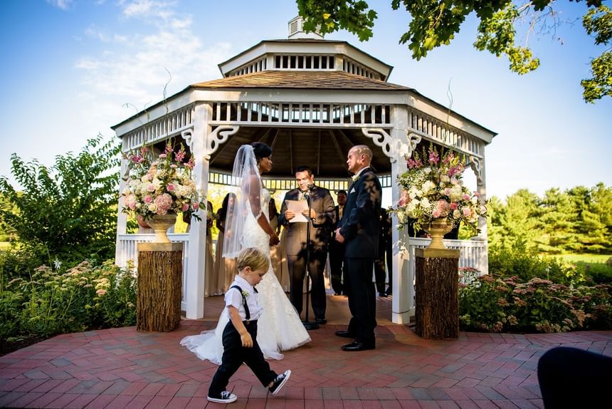 Outdoor wedding taking place in a white gazebo decorated with floral arrangements at Aramark Chauncey Conference Center