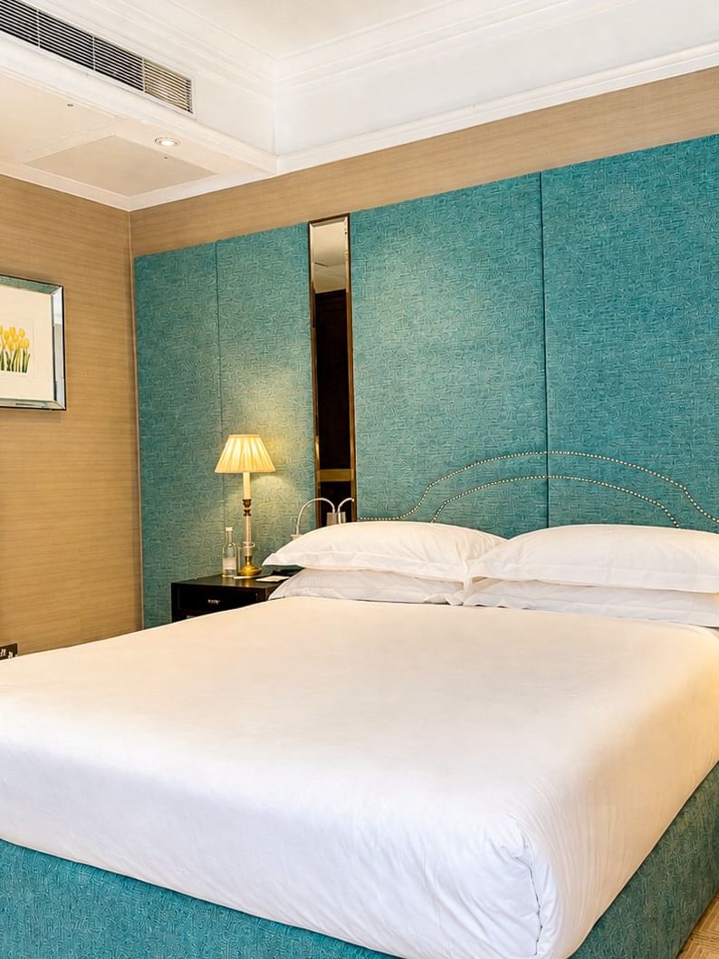 White bed by a large dark wardrobe under a teal textured wall with bedside lamps at Warwick Hotels & Resorts
