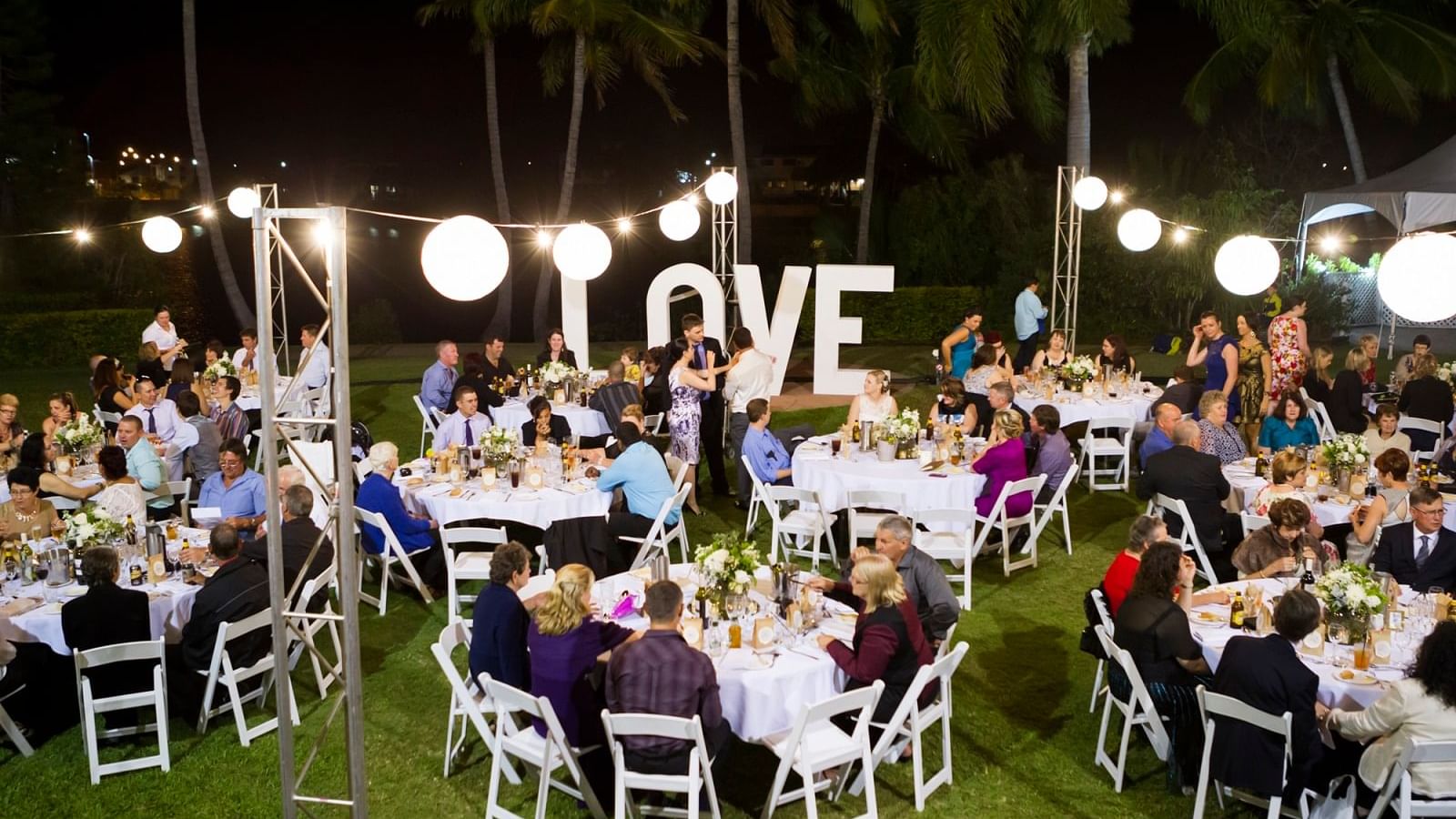 People in an outdoor night event with a love sign & hanging lights at Mercure Hotel Townsville