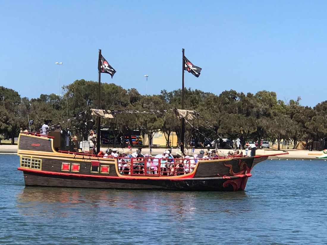 Mandurah Pirate Ship with black flags sails on the water carrying passengers near The Sebel Mandurah