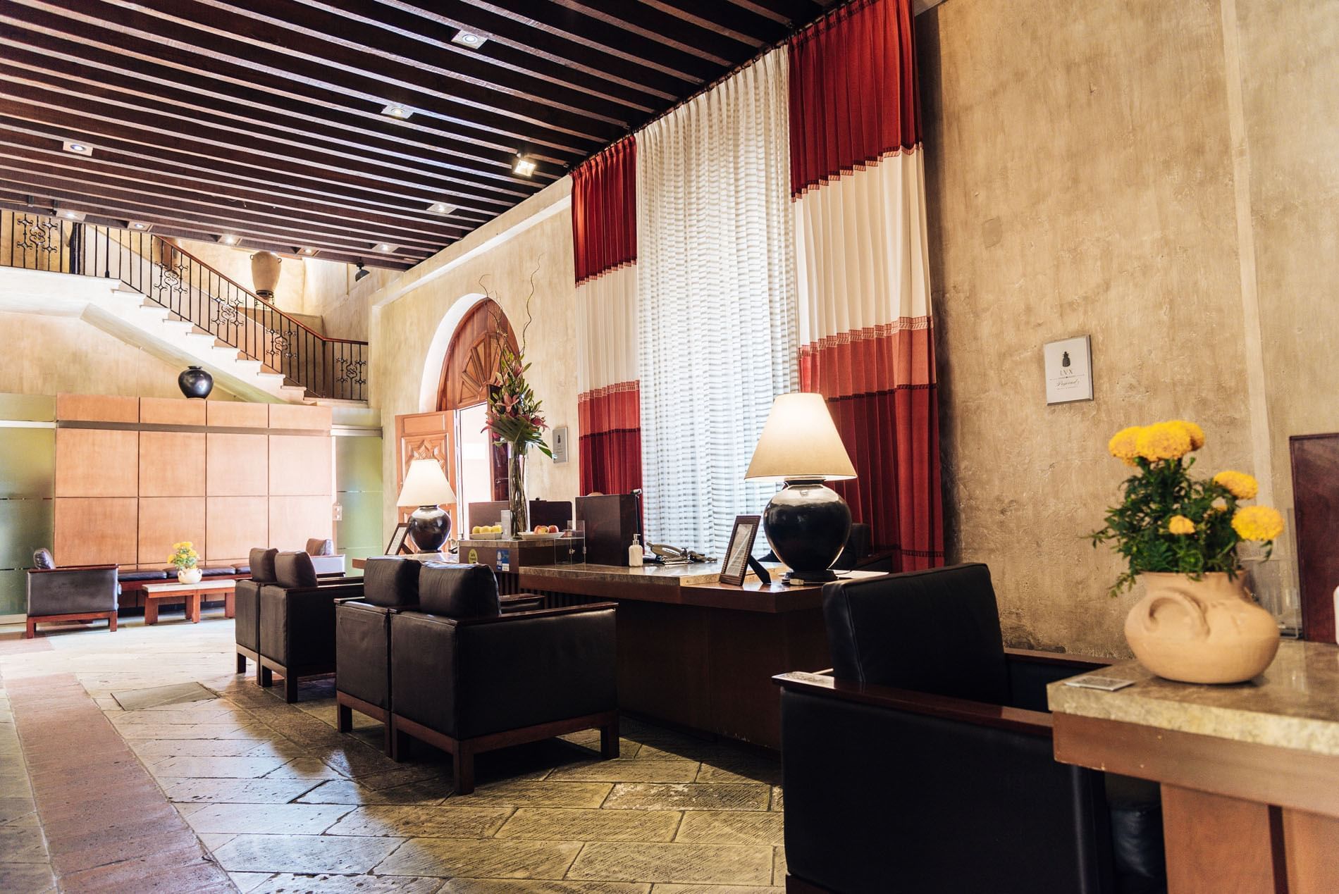 Elegant lobby with dark leather chairs, a wooden desk, and vibrant flowers at Quinta Real Oaxaca