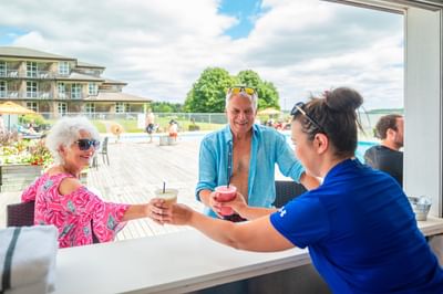 Couple ordering drinks by an outdoor pool bar area near the sunny pool deck at Rodd Brudenell River Resort
