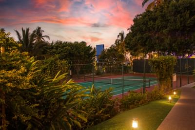 Cancha de tenis rodeada de vegetación exuberante, iluminada con luces suaves en el Sunset Plaza Beach Resort, uno de los mejores hoteles con vistas a la playa en Puerto Vallarta