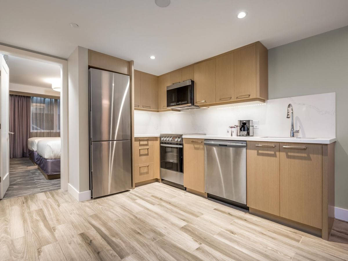 View of the full kitchen with oven, microwave, fridge, dishwasher and sink, with a view into the second bedroom