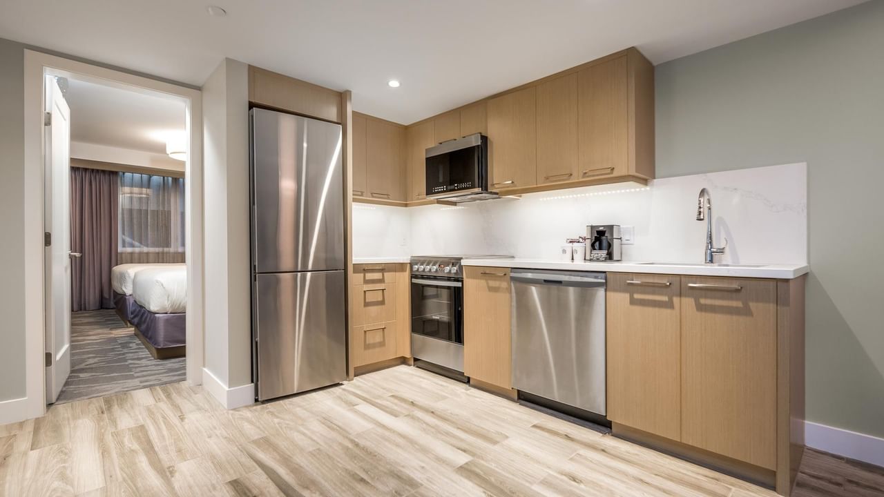 View of the full kitchen with oven, microwave, fridge, dishwasher and sink, with a view into the second bedroom