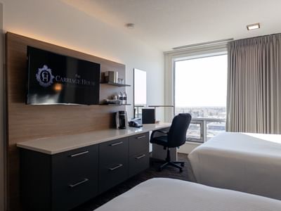 Two beds, work area with chair, large window, and flat screen TV in a Carriage House room