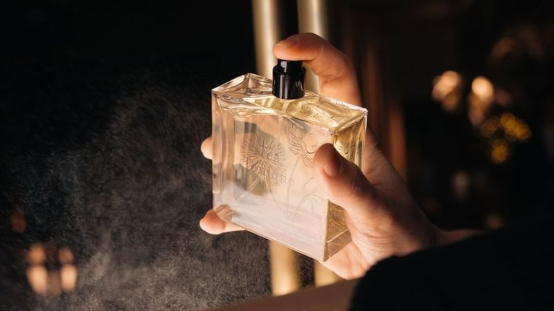 Close-up of a hand holding and spraying a luxurious perfume bottle at The Londoner Hotel
