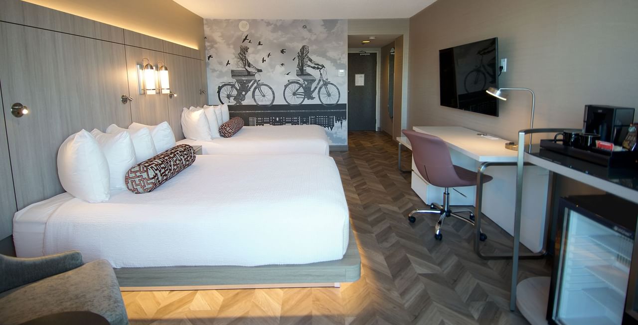 Hotel guestroom with two queen beds, TV, coffee machine, work desk, and minifridge