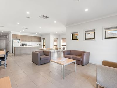 Open lounge area with sofas, tables, and a kitchen at La Trobe University Regional Housing – Mildura.