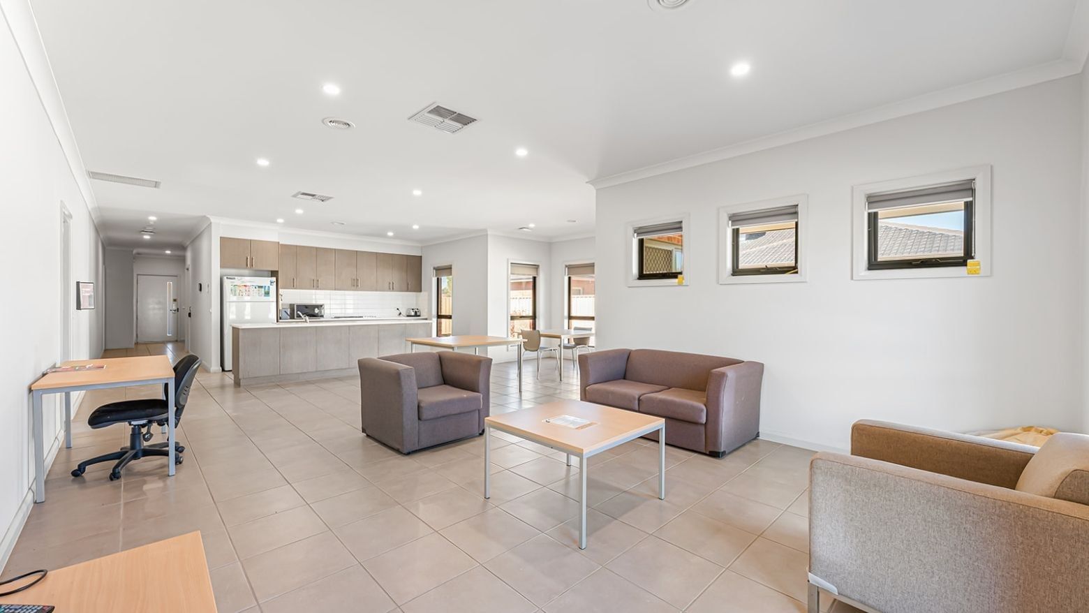 Open lounge area with sofas, tables, and a kitchen at La Trobe University Regional Housing – Mildura.