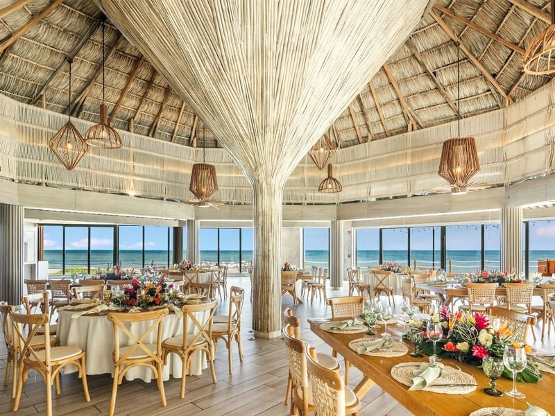 An elegant, beachside banquet hall with wooden tables and chairs, adorned with flowers at Grand Fiesta Americana Veracruz.