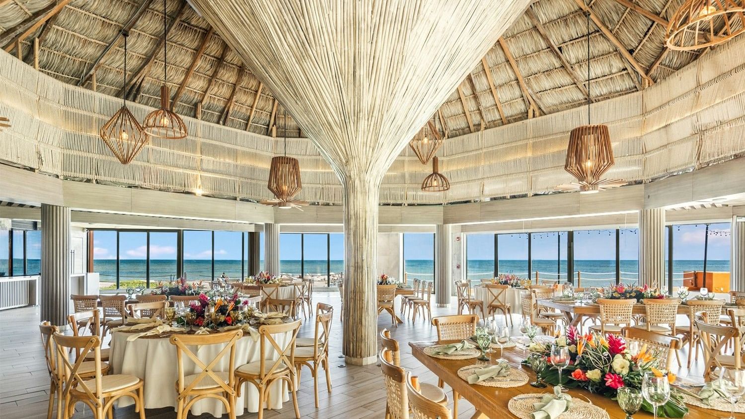 An elegant, beachside banquet hall with wooden tables and chairs, adorned with flowers at Grand Fiesta Americana Veracruz.
