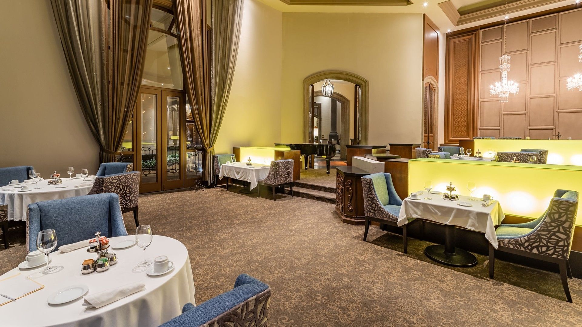 Tierra Mía dining area with a grand piano in the background and refined table settings at Quinta Real Monterrey