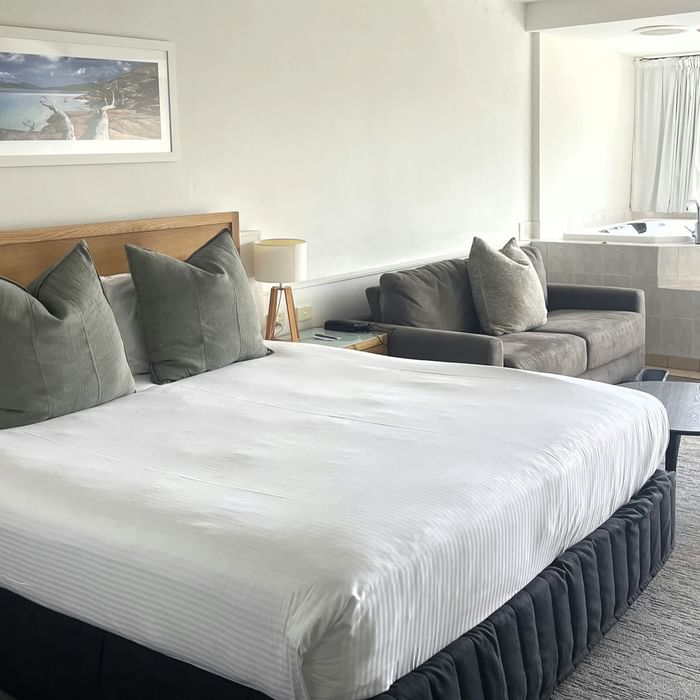 A bedroom with a king bed, couch, coffee table, and bathroom at Mercure Charlestown.