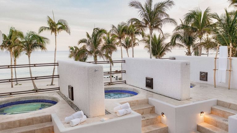 Oceanfront spa treatment pools with white walls, palm trees, and ocean views.