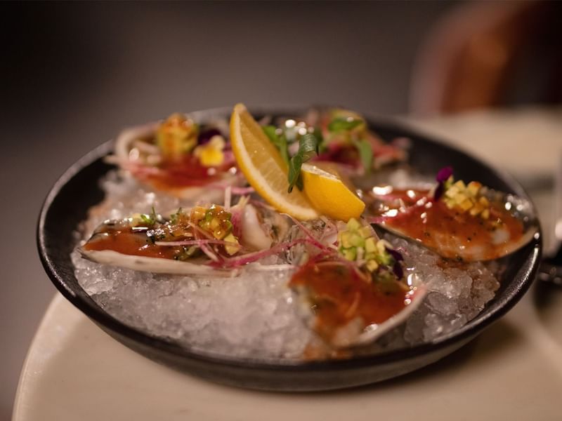 Plate of fresh oysters on ice, garnished with sauces, herbs, and lemon slices, at Live Aqua San Miguel de Allende