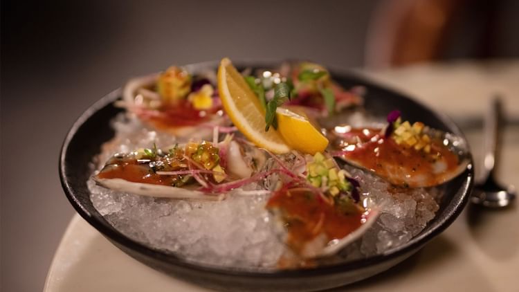 Plate of fresh oysters on ice, garnished with sauces, herbs, and lemon slices, at Live Aqua San Miguel de Allende