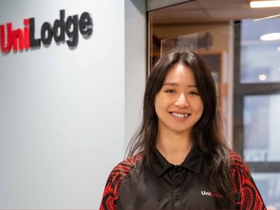 Smiling woman in UniLodge shirt standing by the UniLodge wall.