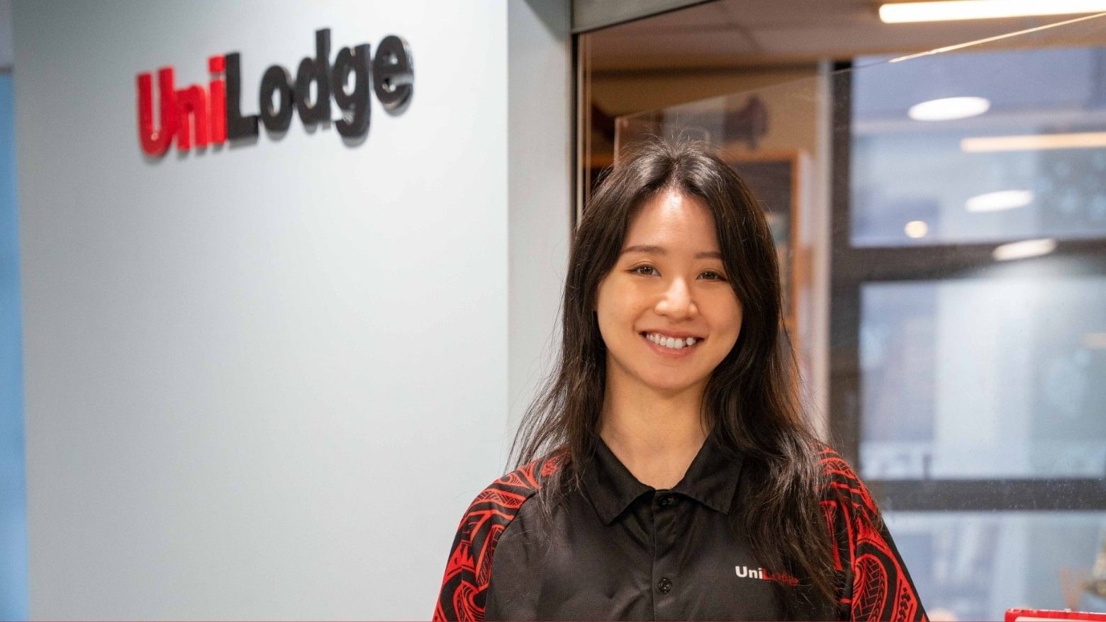 Smiling woman in a black UniLodge polo shirt standing in front of a wall.