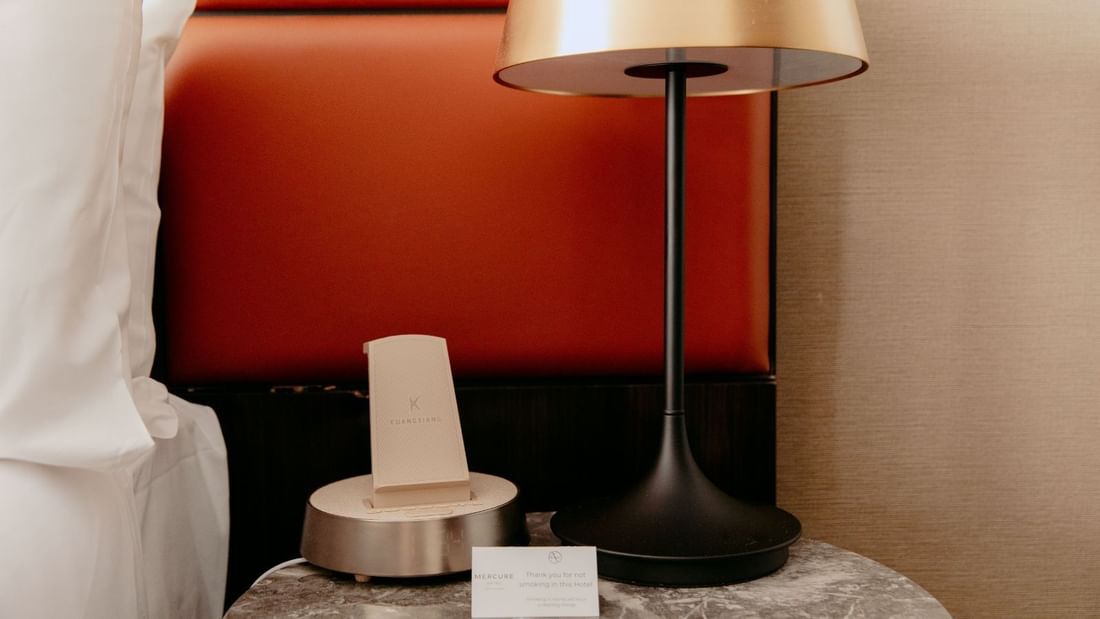 A bedside table with a lamp and a small device with a card on it.