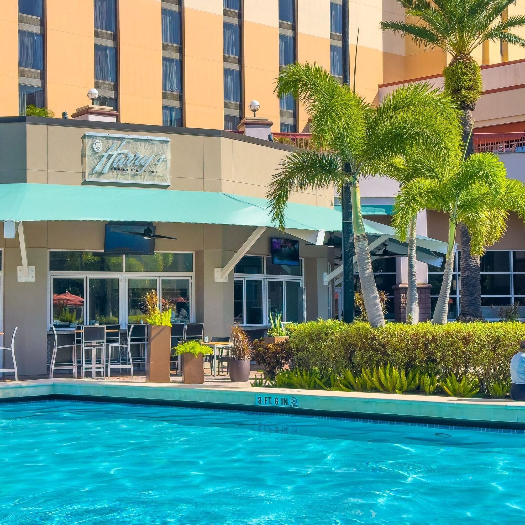 The exterior of a restaurant called Harrys with a blue awning, sitting beside a blue swimming pool.