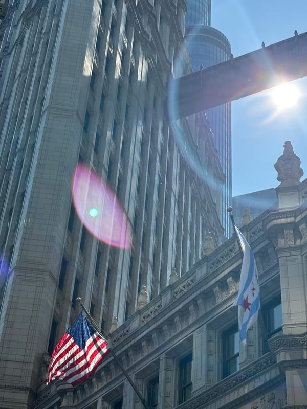 American and Chicago flags against clear sky & sunlight flare between two buildings near Warwick Allerton Chicago
