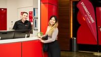 Two staff members smiling at a modern red and white reception desk with StudentLiving by UniLodge branding visible.