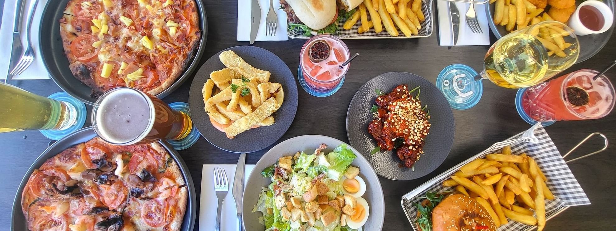 Food spread featuring pizza, wings, salad, and drinks on a table in Celsius Restaurant & Bar at Mercure Hotel Townsville