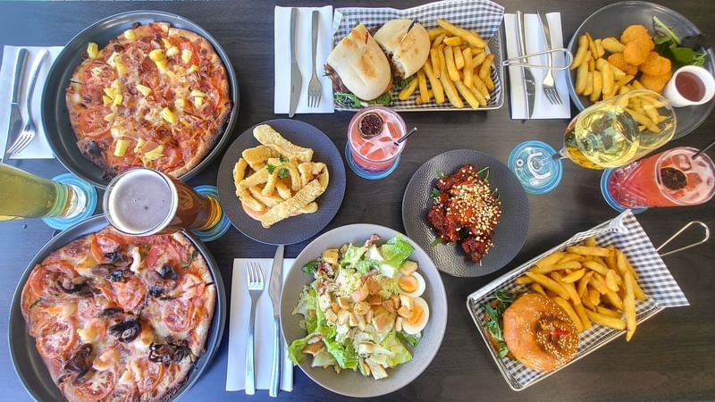 Food spread featuring pizza, wings, salad, and drinks on a table in Celsius Restaurant & Bar at Mercure Hotel Townsville