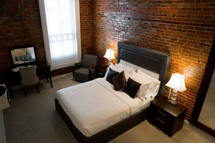 queen bed with two red accent pillows with exposed brick wall