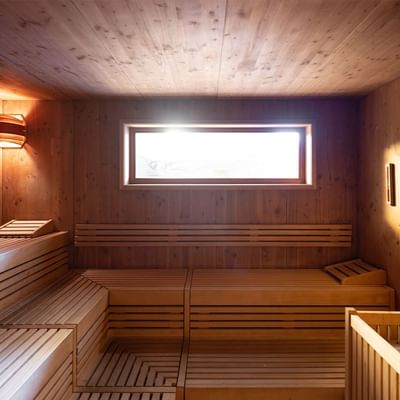 Wooden sauna with a large window allowing natural light at Falkensteiner Hotel Antholz