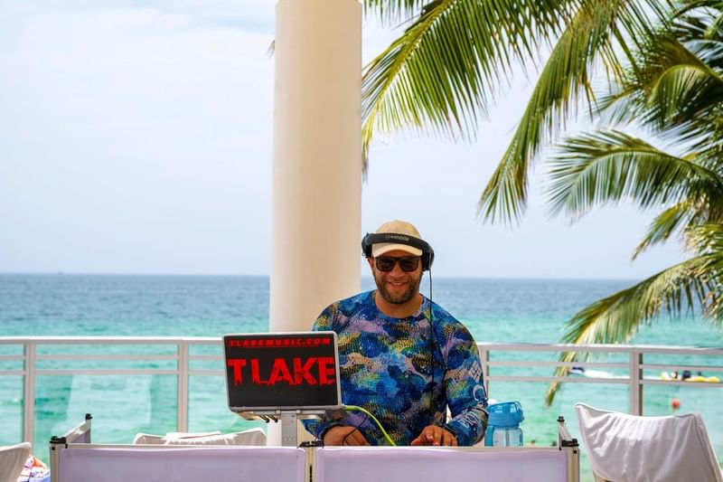 DJ with headphones spinning tracks on a laptop table, with the ocean behind, at The Diplomat Resort