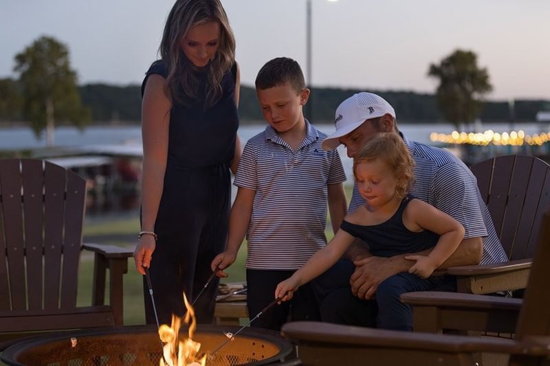 Family with two young children roasting marshmallows over a stone fire pit at dusk at Shangri-La Resort and Golf Club