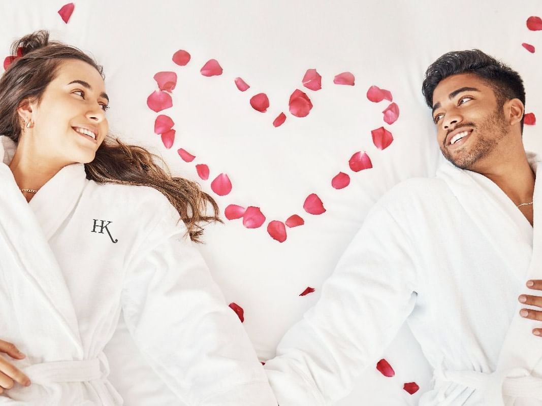 Couple in robes on a bed surrounded by petals in a heart shape promoting love stories.