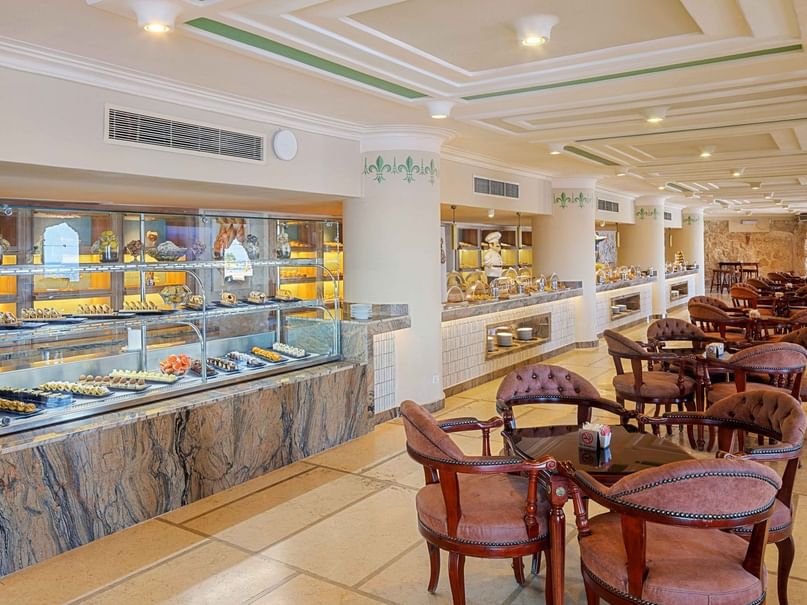 Elegant restaurant interior with marble counters, assorted desserts, and many round tables with chairs.