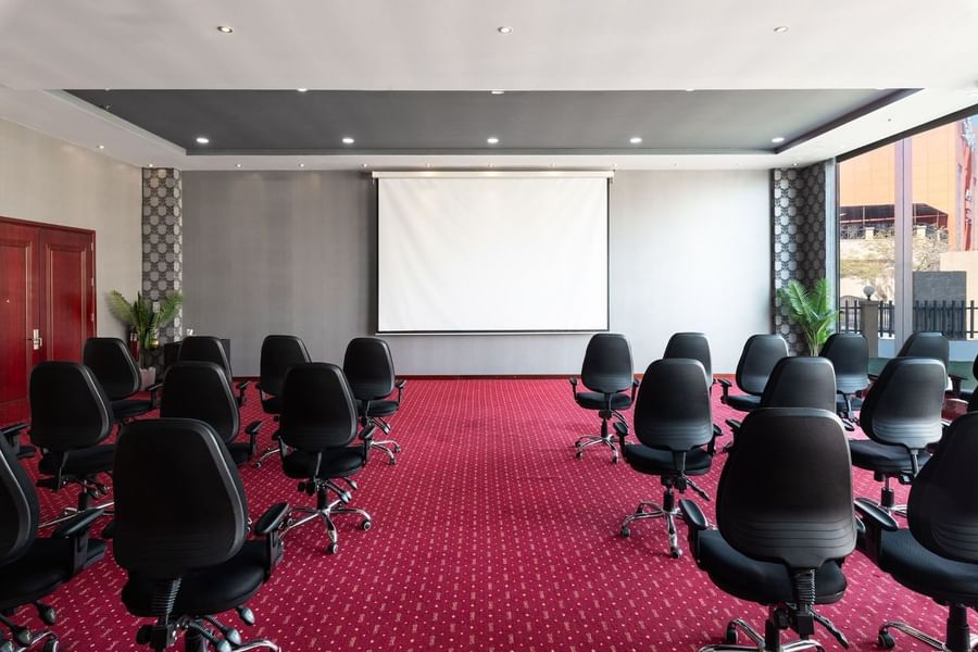 Black office chairs facing a white projector screen on a red patterned carpet in Crystal B at Warwick Al Jubail