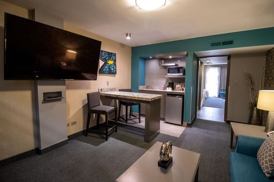 Sala con TV de pared y barra de cocina junto a sofá turquesa y mesa de centro en Suite de Araiza Mexicali