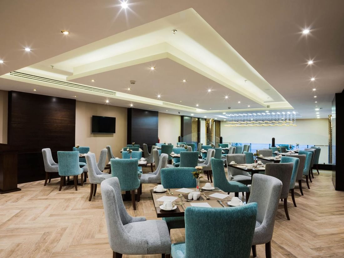 Blue armchairs by square dining tables under a recessed ceiling in Naviti Restaurant at Naviti By Warwick Dammam