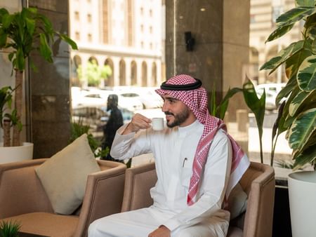 Man in traditional attire sipping coffee at Oasis Coffee Shop in Saja by Warwick Madinah.