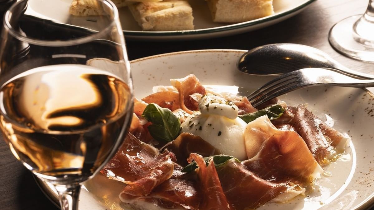 Prosciutto and mozzarella with basil, beside a glass of wine served in Di Francesco Cucina at Crown Hotel Melbourne