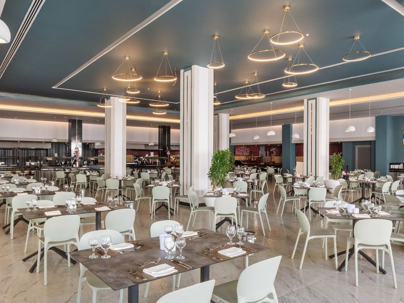 An empty restaurant with many tables and chairs, blue ceiling, white pillars, and round light fixtures.