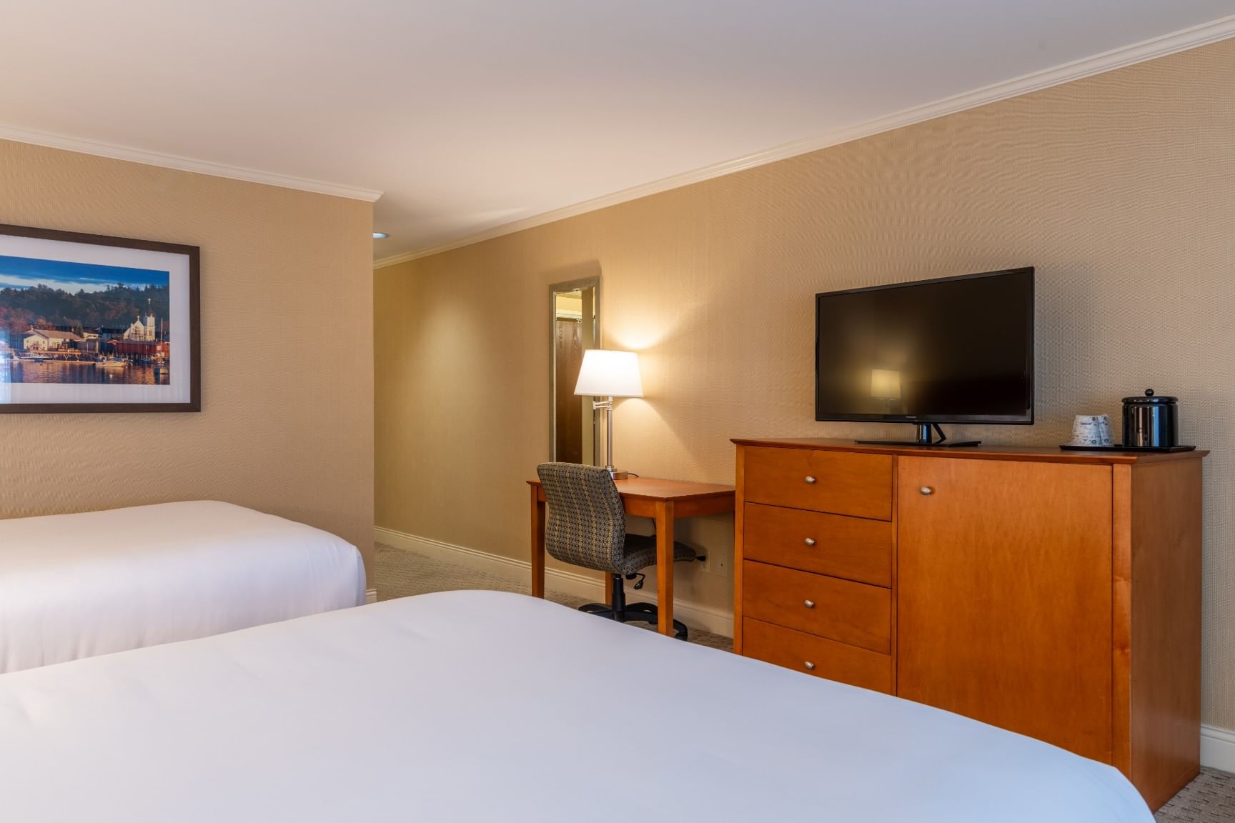 A hotel room with two queen beds, a desk, TV, and dresser.