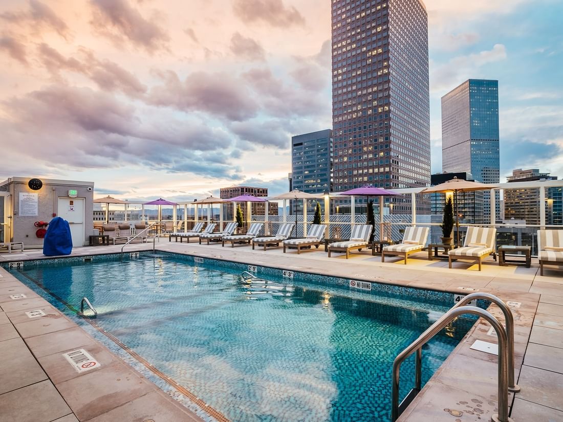 Rooftop swimming pool with striped loungers under umbrellas by city skyscrapers in Pool Bar (Seasonal) at Warwick Denver