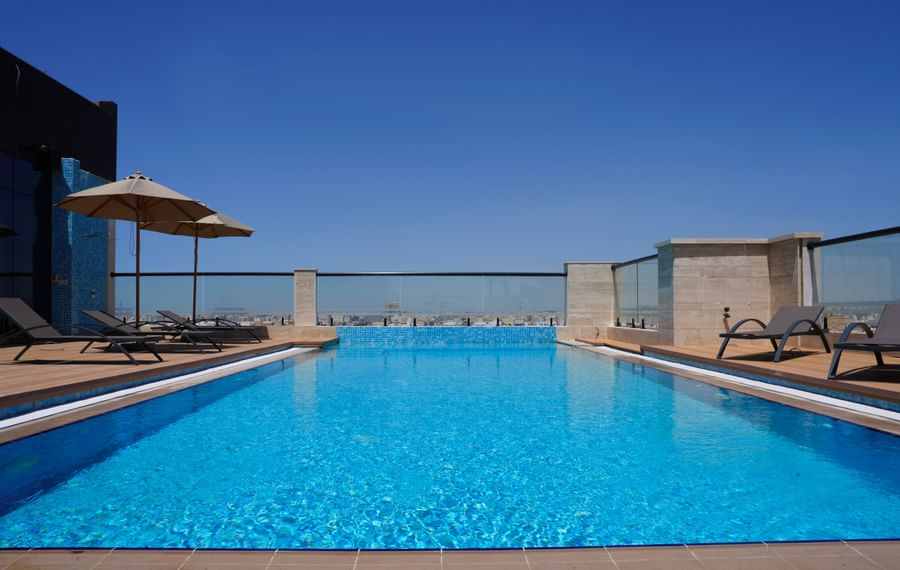 Clear blue pool with lounge chairs and umbrellas on the rooftop at Warwick Hotel & Spa.